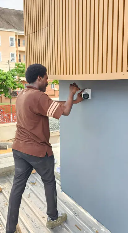 technician actively installing a security camera on the exterior of a modern building